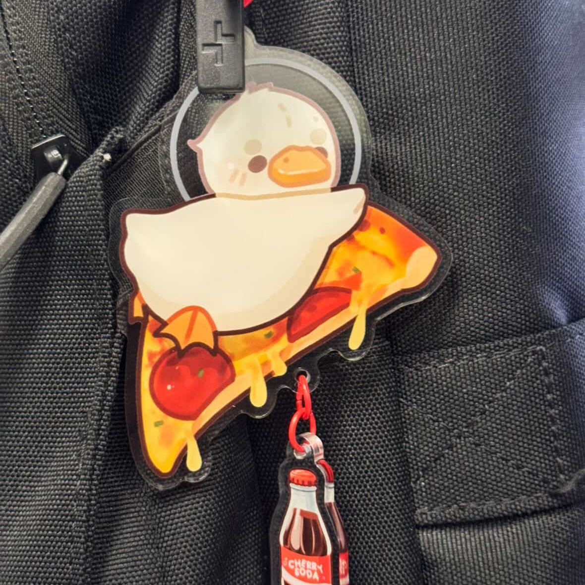 Keychain with cartoon duck on pizza and Coca-Cola bottle on a black backpack